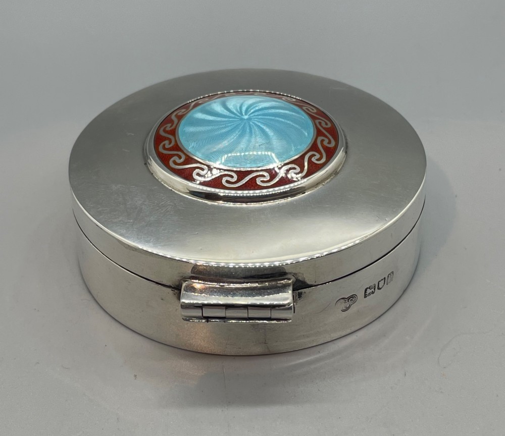 A circular sterling silver trinket box featuring a central light blue guilloche enamel medallion encircled by a red enamel border. View V