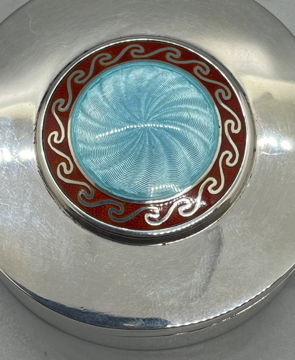 A circular sterling silver trinket box featuring a central light blue guilloche enamel medallion encircled by a red enamel border. View VII