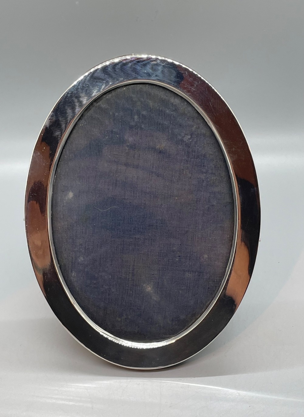 A George V oval sterling silver photo frame featuring a plain polished silver border and a dark wood easel backing. View II