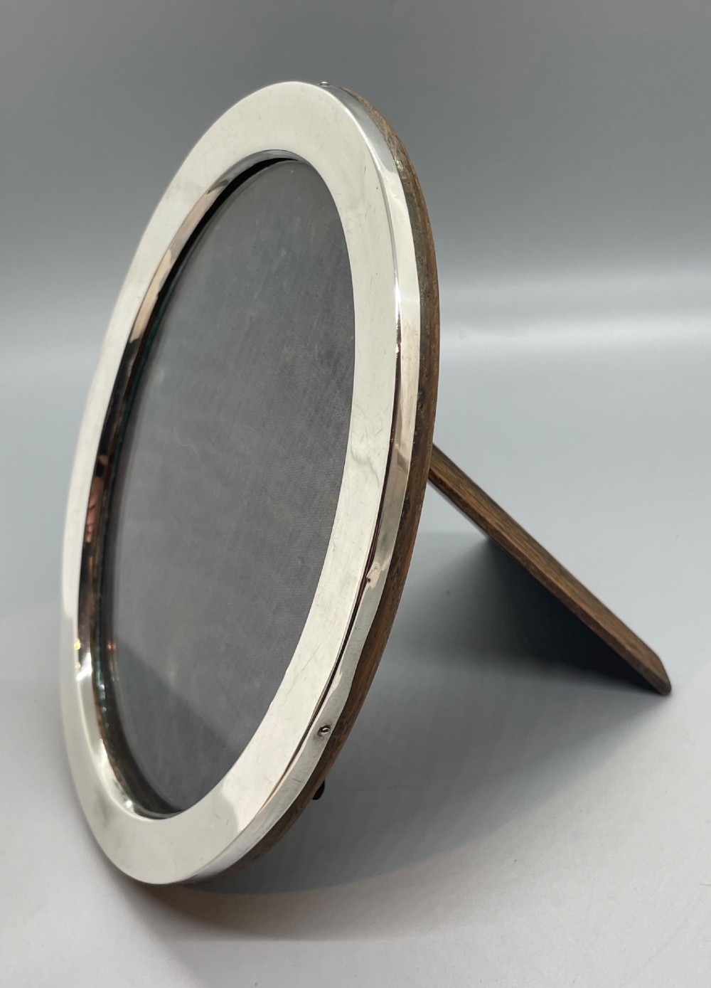 A George V oval sterling silver photo frame featuring a plain polished silver border and a dark wood easel backing. View VIII