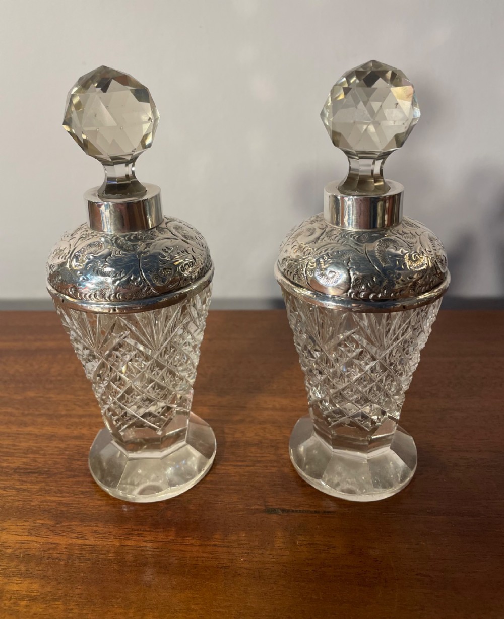 A pair of George V cut glass scent bottles featuring embossed sterling silver mounts and faceted glass stoppers. View XIII
