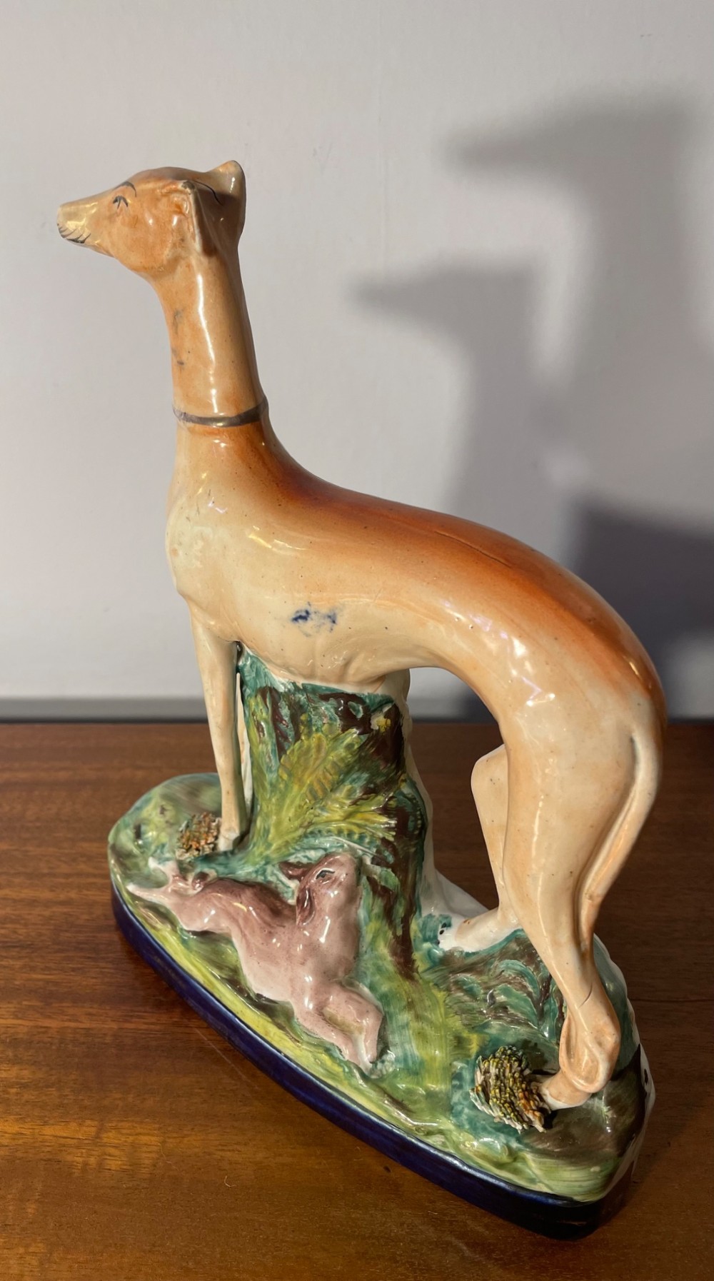 An antique Staffordshire earthenware figure depicting a standing tan hound with a crouching hare on a green and blue glazed base. View IV