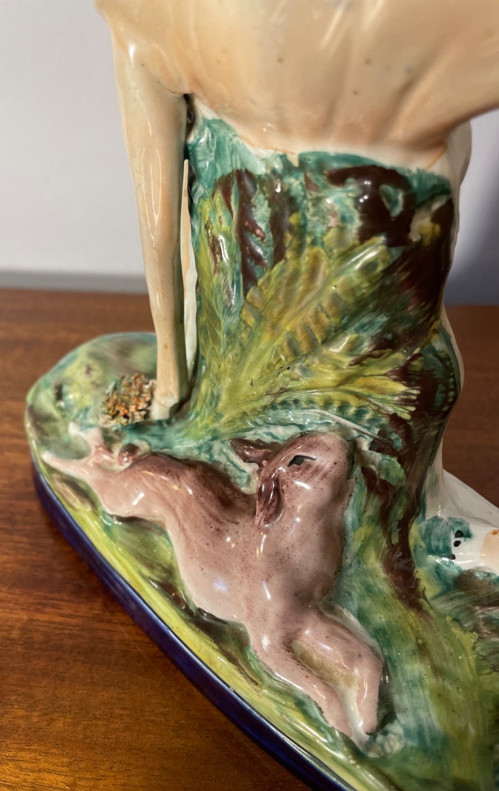 An antique Staffordshire earthenware figure depicting a standing tan hound with a crouching hare on a green and blue glazed base. View V