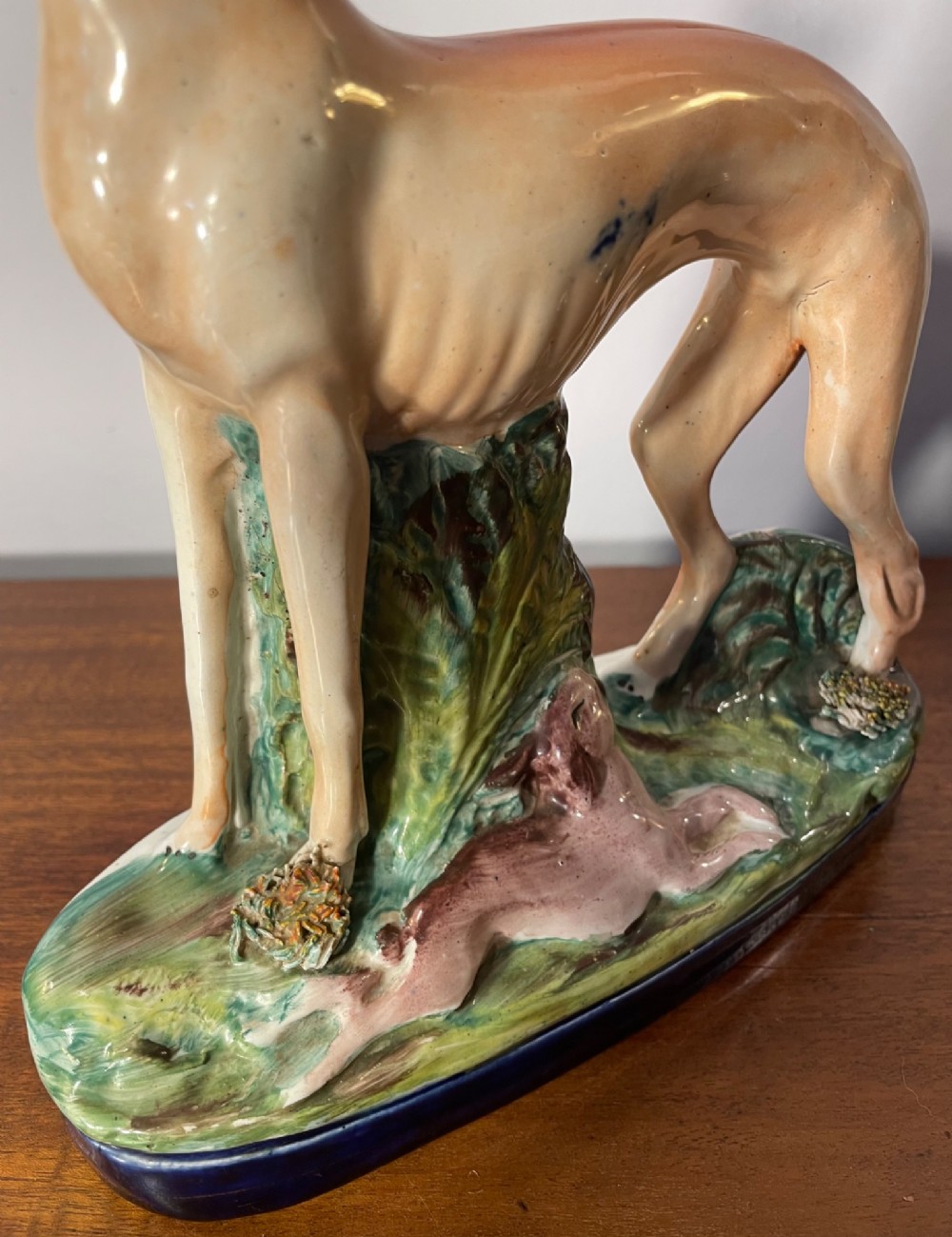 An antique Staffordshire earthenware figure depicting a standing tan hound with a crouching hare on a green and blue glazed base. View VI