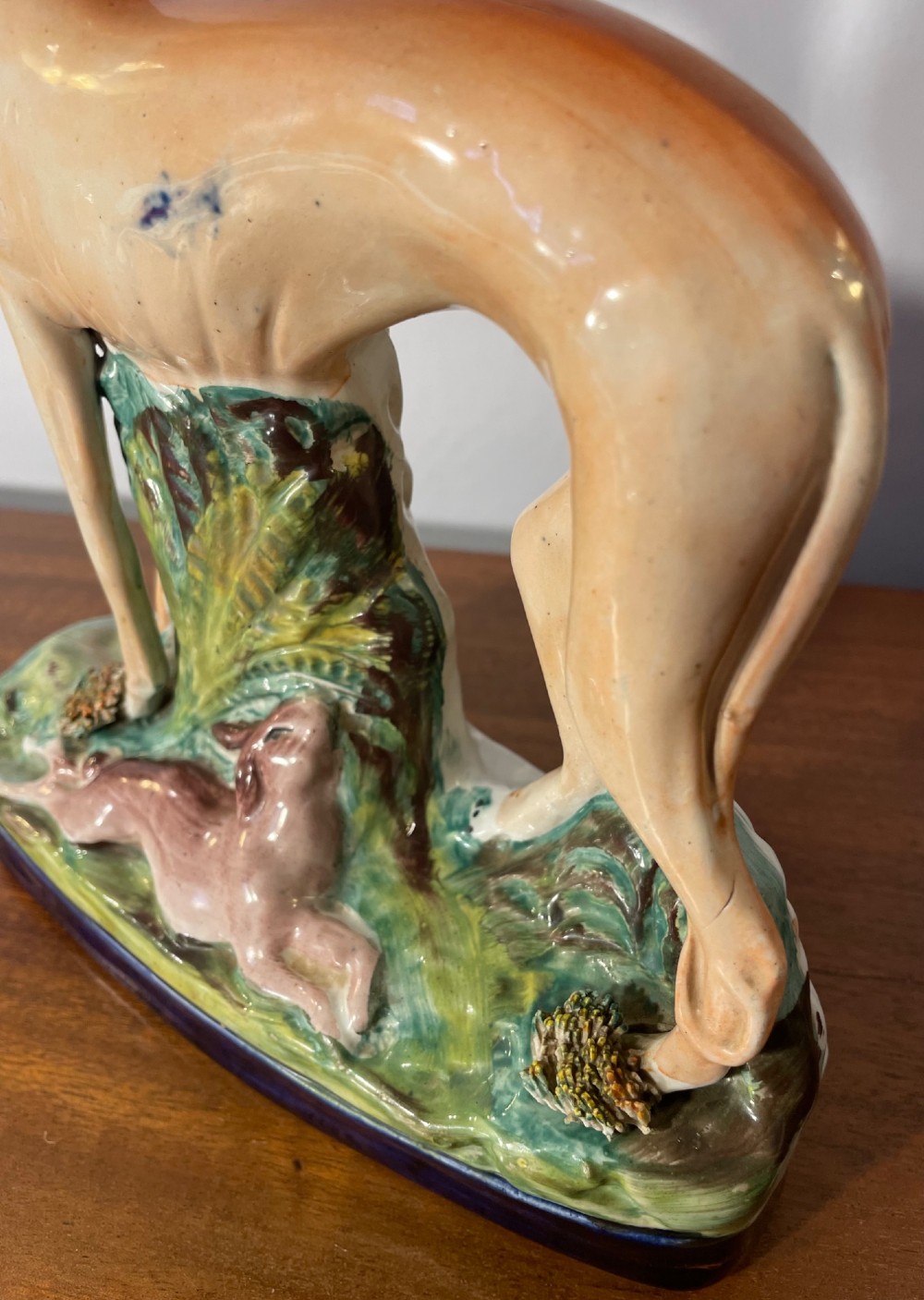 An antique Staffordshire earthenware figure depicting a standing tan hound with a crouching hare on a green and blue glazed base. View VIII