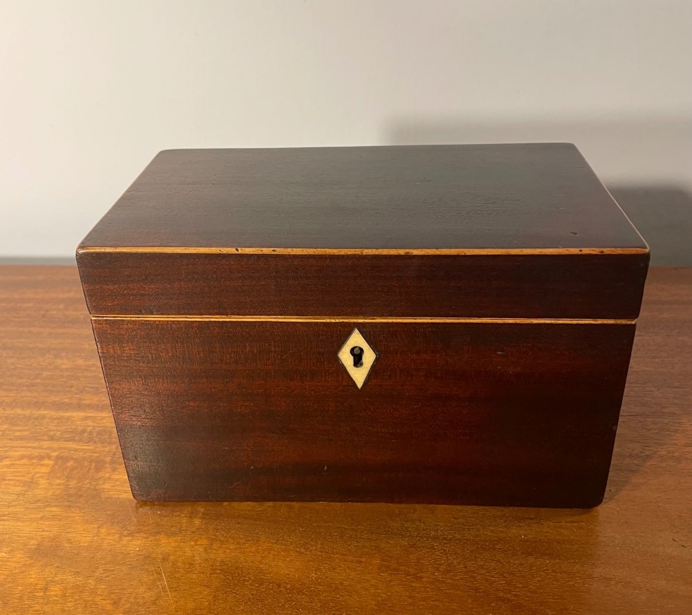 A rectangular Georgian dark mahogany tea caddy featuring delicate boxwood edge stringing and a diamond-shaped bone escutcheon on the front panel. View IX