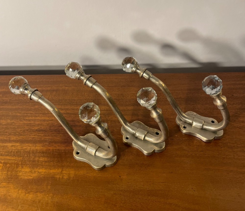 A set of three antique French brass coat hooks featuring faceted clear glass finials on curved double arms.