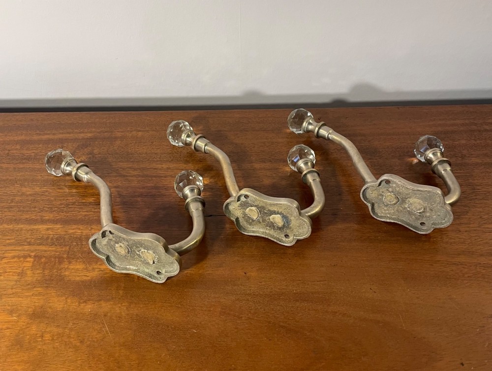 A set of three antique French brass coat hooks featuring faceted clear glass finials on curved double arms. View II