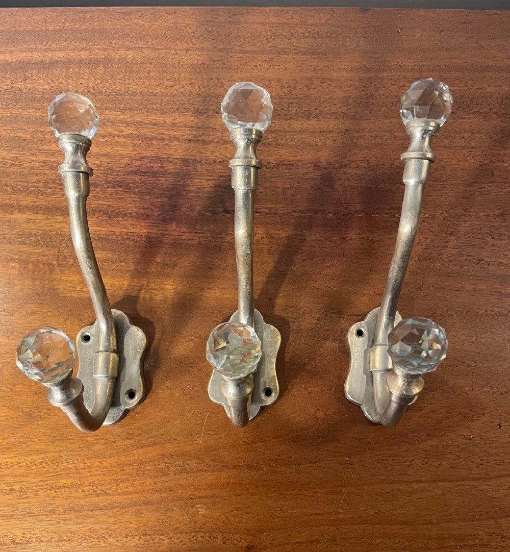 A set of three antique French brass coat hooks featuring faceted clear glass finials on curved double arms. View III