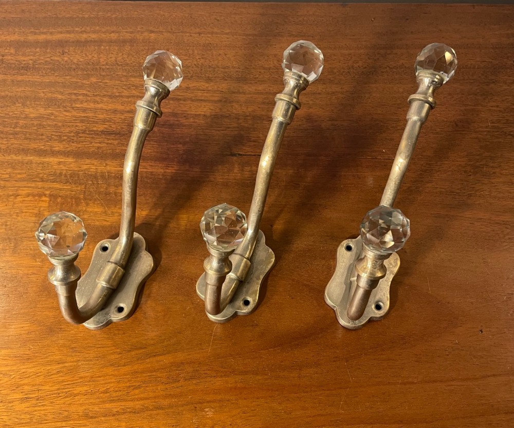 A set of three antique French brass coat hooks featuring faceted clear glass finials on curved double arms. View IV