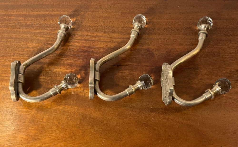 A set of three antique French brass coat hooks featuring faceted clear glass finials on curved double arms. View VI