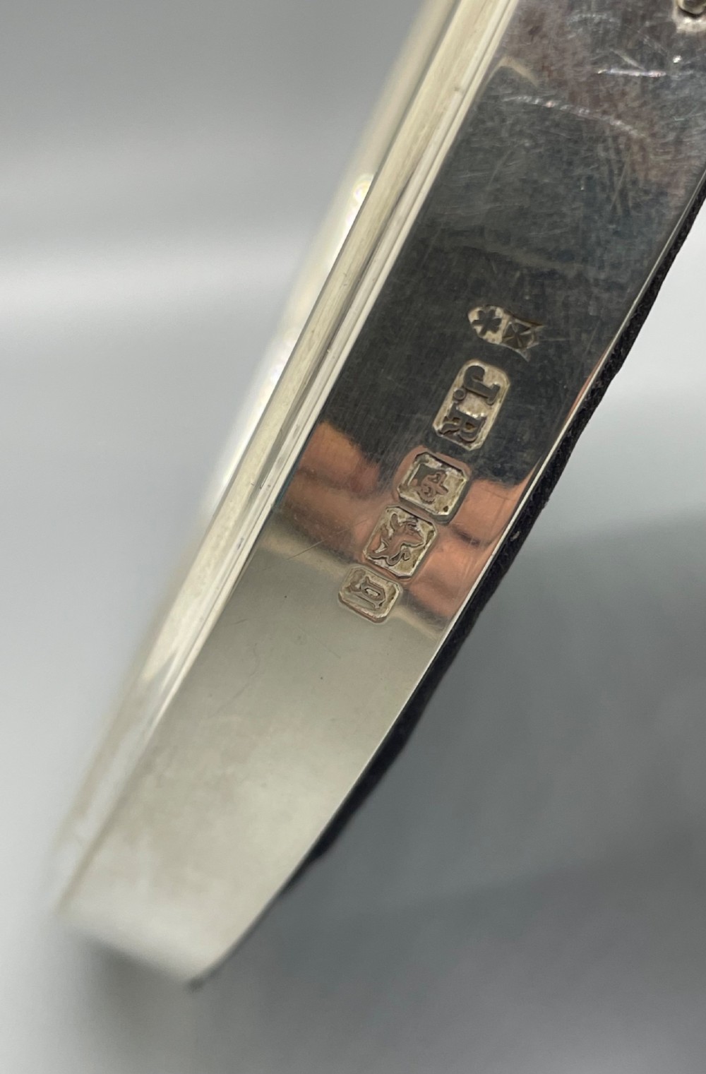 An oval sterling silver photo frame featuring a crest decorated with a ribbon bow, containing a dark fabric interior. View VII