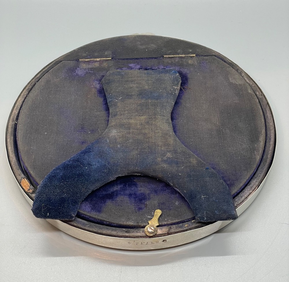 An oval sterling silver photo frame featuring a crest decorated with a ribbon bow, containing a dark fabric interior. View IX