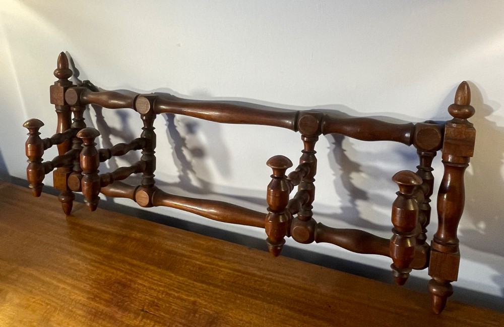 An Edwardian turned mahogany wall-mounted coat rack featuring horizontal spindle rails, four turned pegs, and decorative finials.