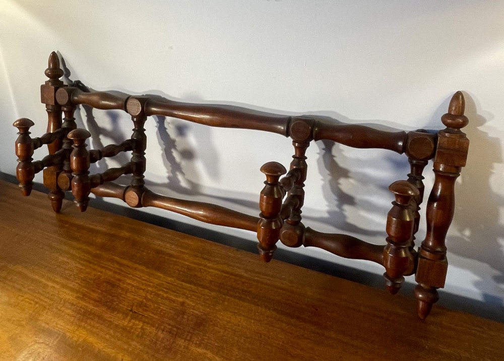 An Edwardian turned mahogany wall-mounted coat rack featuring horizontal spindle rails, four turned pegs, and decorative finials. View II