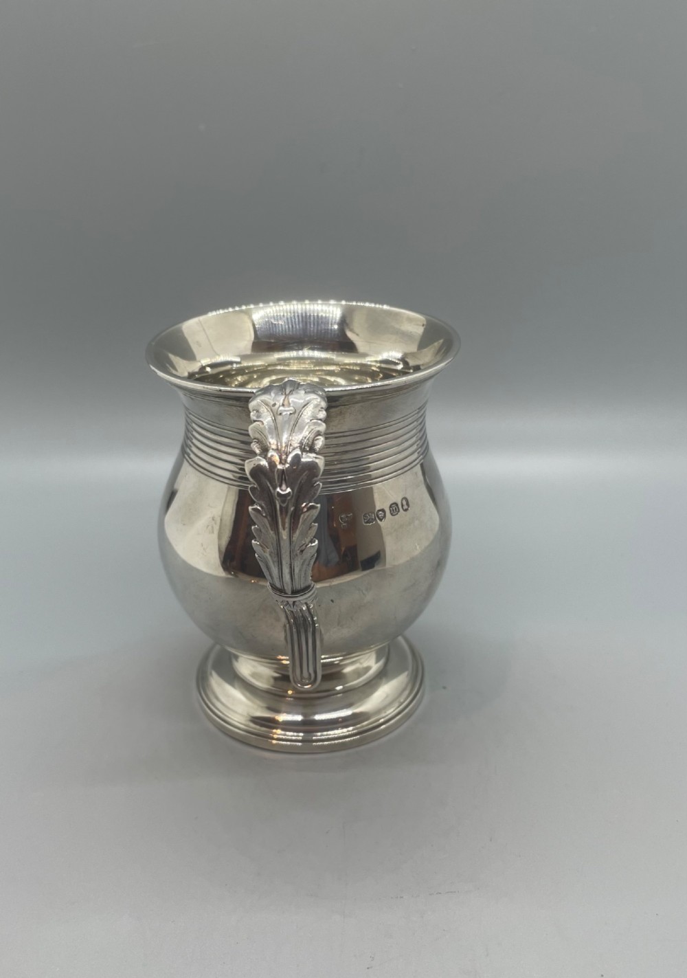 A George IV sterling silver baluster mug featuring a reeded collar, decorative acanthus leaf handle, and a stepped circular pedestal base. View II