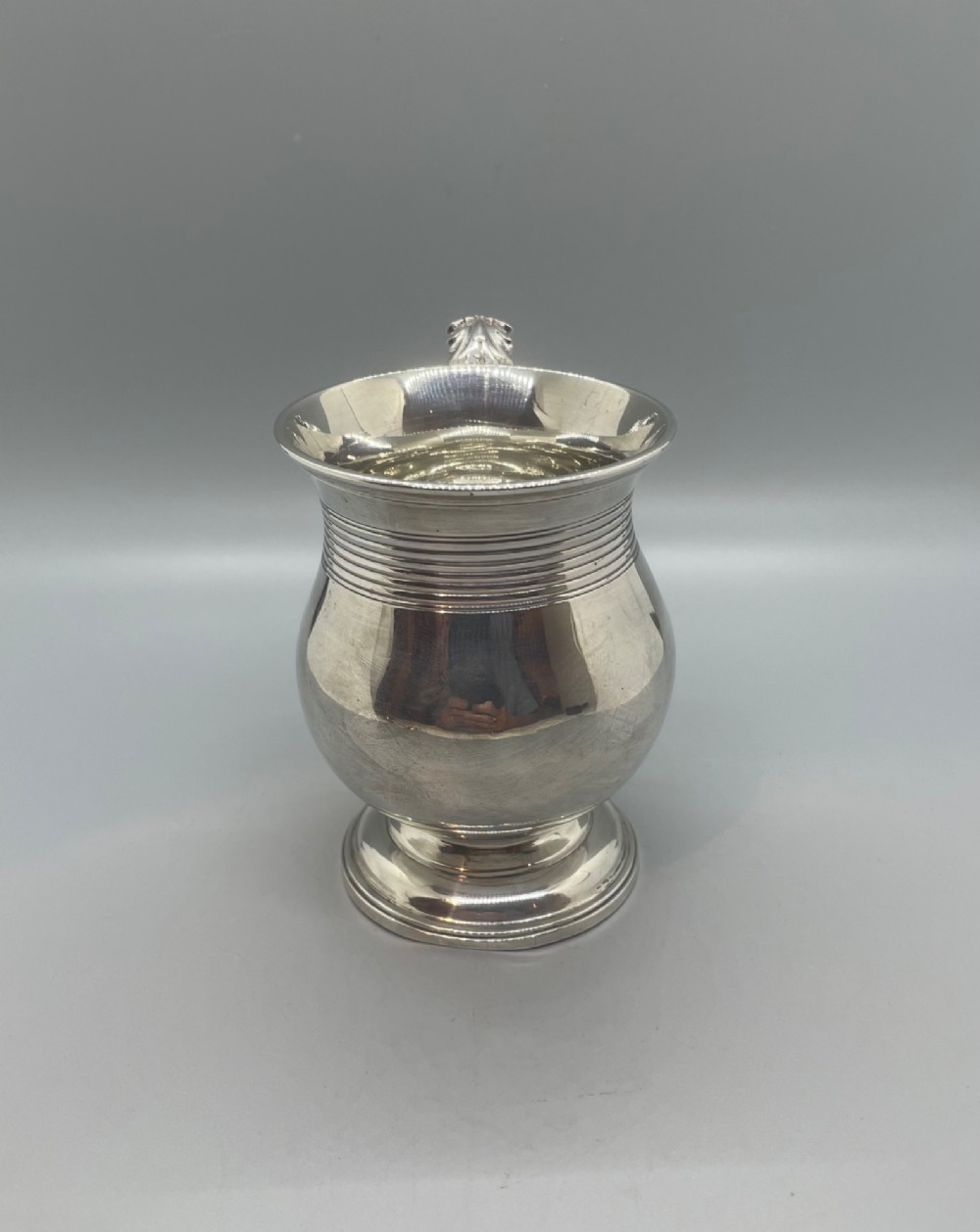 A George IV sterling silver baluster mug featuring a reeded collar, decorative acanthus leaf handle, and a stepped circular pedestal base. View IV