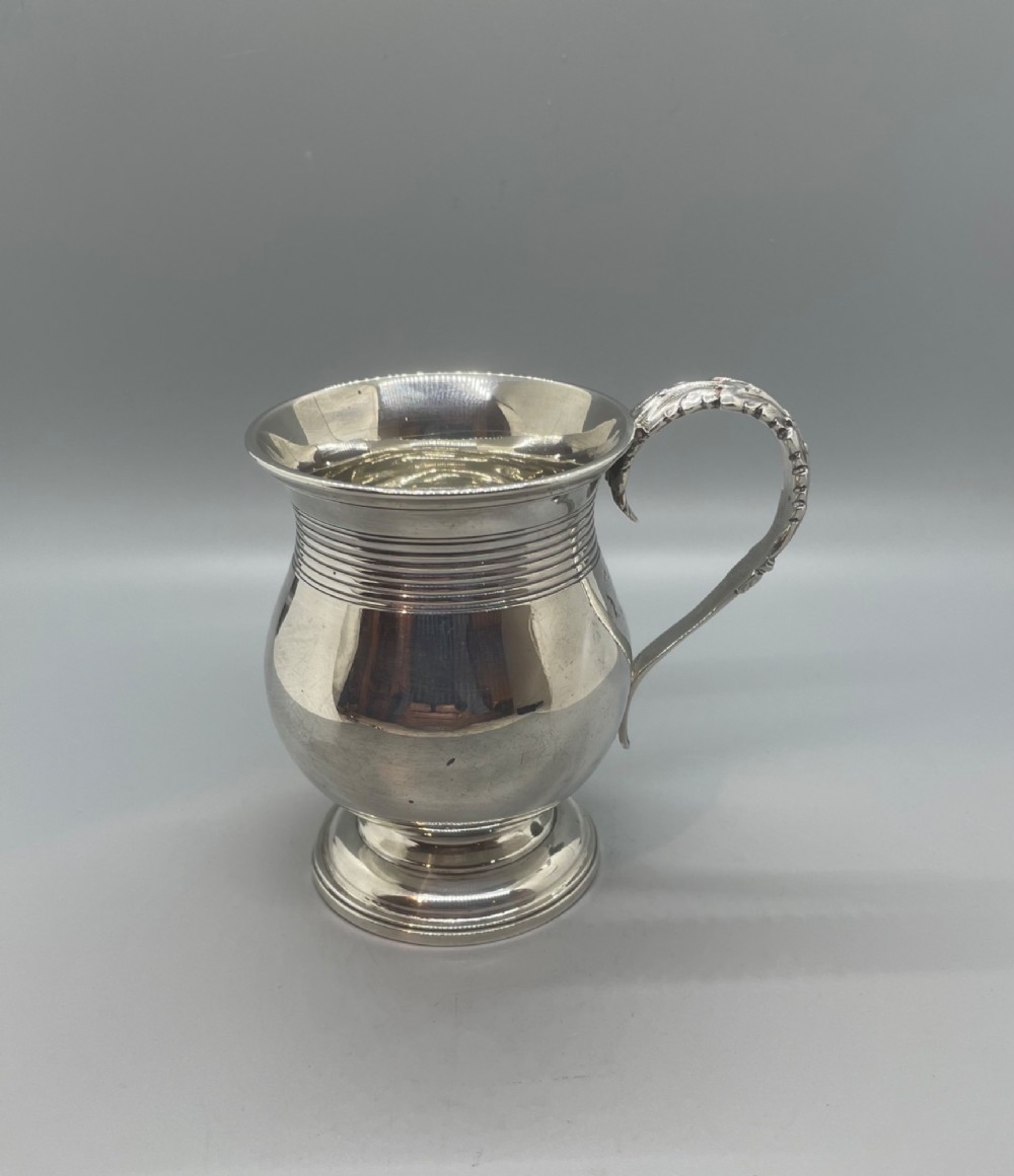 A George IV sterling silver baluster mug featuring a reeded collar, decorative acanthus leaf handle, and a stepped circular pedestal base. View V