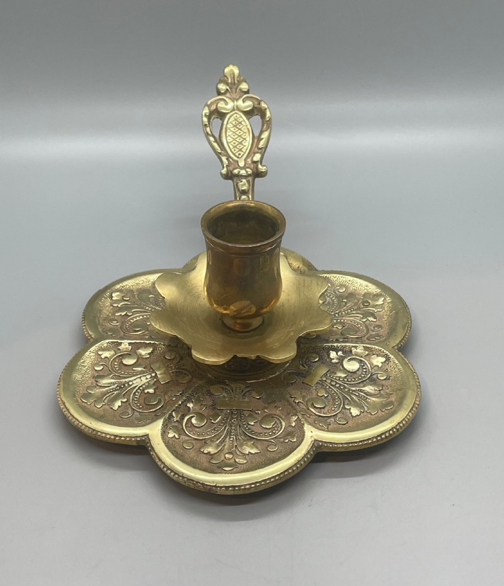 Late 19th-century French brass chamberstick featuring a scalloped petal tray with embossed scroll motifs, a central nozzle, and a cast ornate side handle. View II