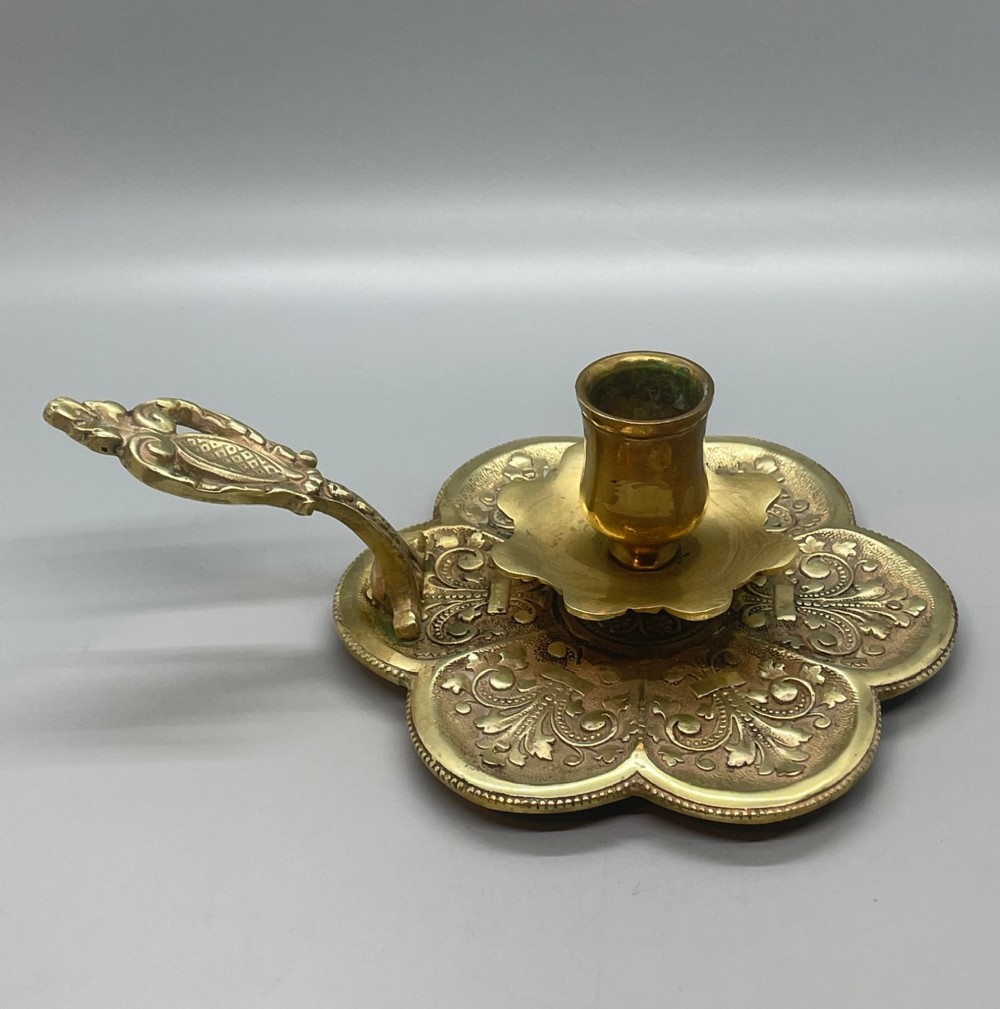 Late 19th-century French brass chamberstick featuring a scalloped petal tray with embossed scroll motifs, a central nozzle, and a cast ornate side handle. View III