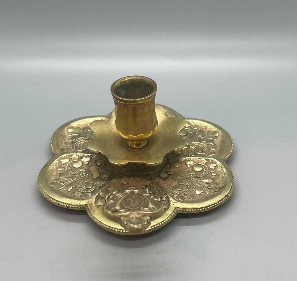 Late 19th-century French brass chamberstick featuring a scalloped petal tray with embossed scroll motifs, a central nozzle, and a cast ornate side handle. View IV