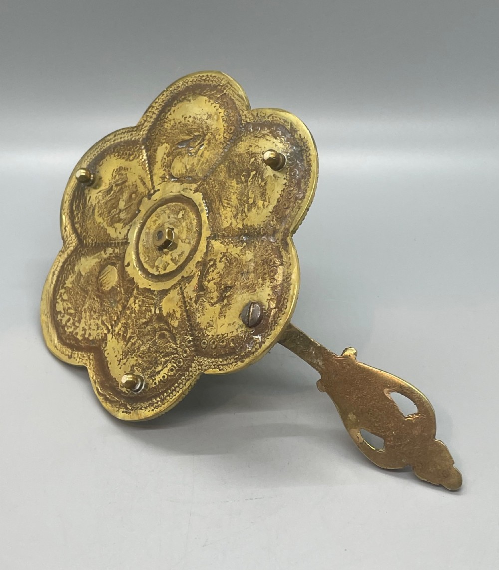 Late 19th-century French brass chamberstick featuring a scalloped petal tray with embossed scroll motifs, a central nozzle, and a cast ornate side handle. View V