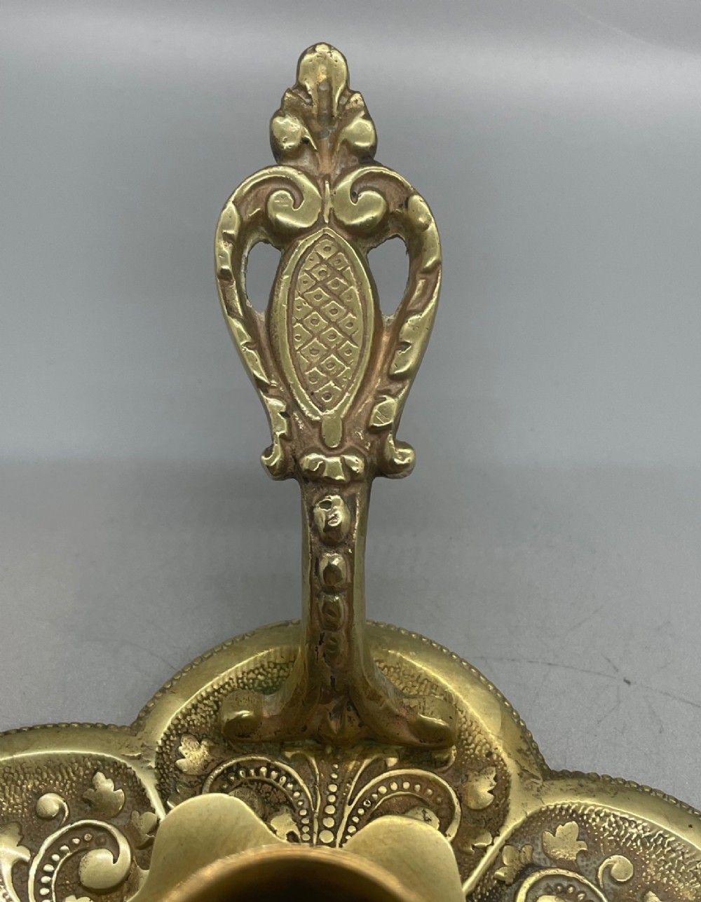 Late 19th-century French brass chamberstick featuring a scalloped petal tray with embossed scroll motifs, a central nozzle, and a cast ornate side handle. View VII