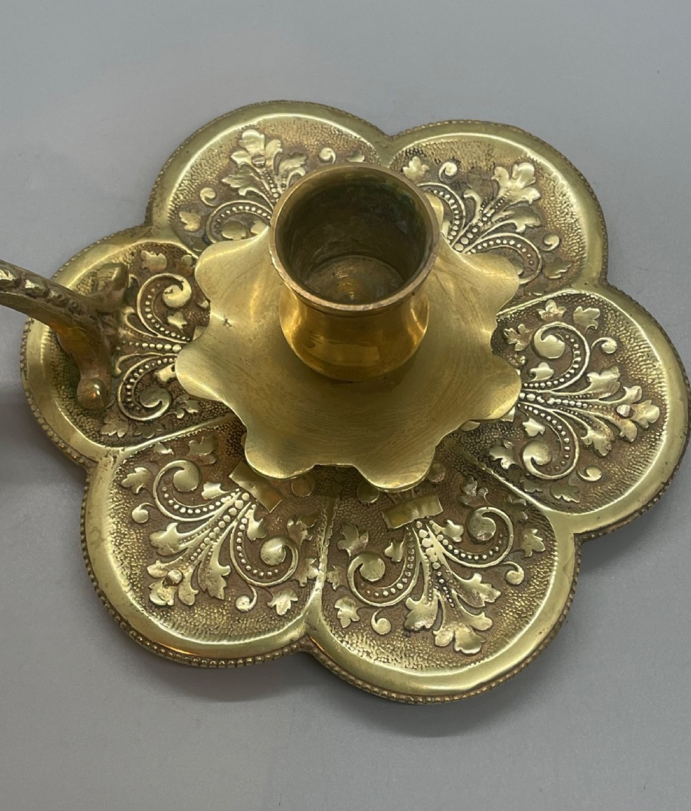 Late 19th-century French brass chamberstick featuring a scalloped petal tray with embossed scroll motifs, a central nozzle, and a cast ornate side handle. View VIII