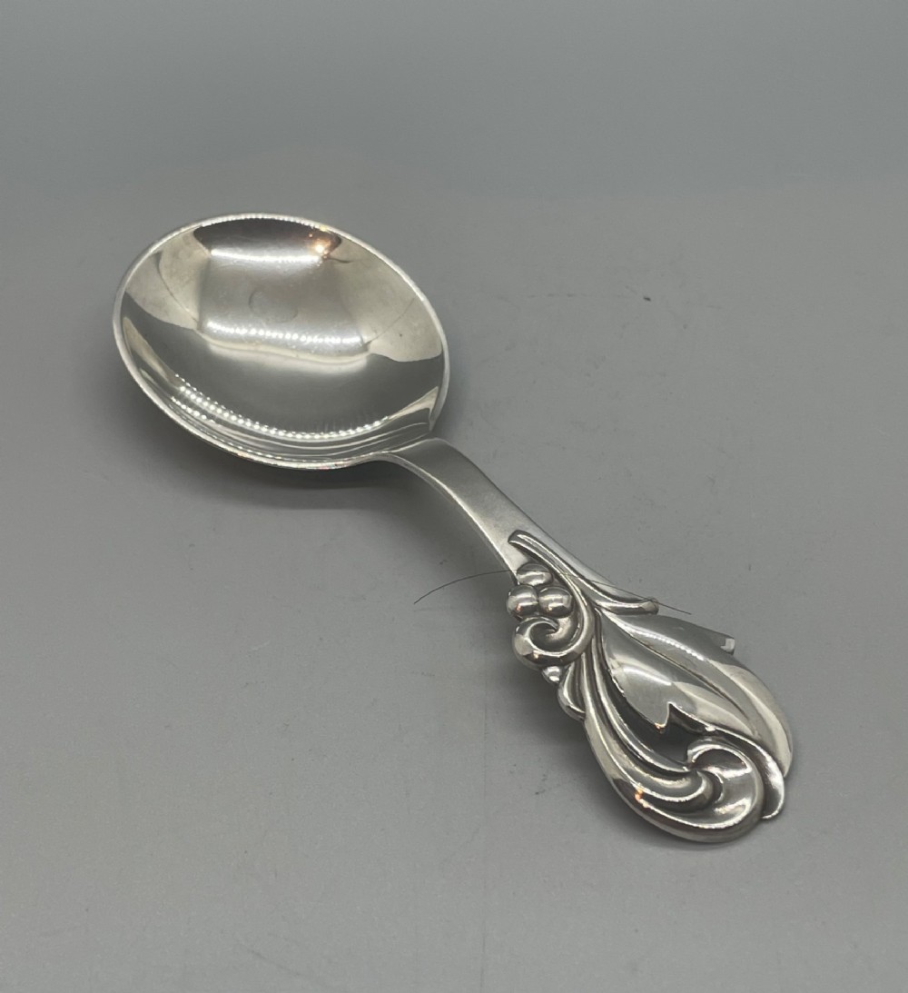 A vintage solid silver caddy spoon featuring a rounded bowl and an ornate leaf and scroll decorated handle.