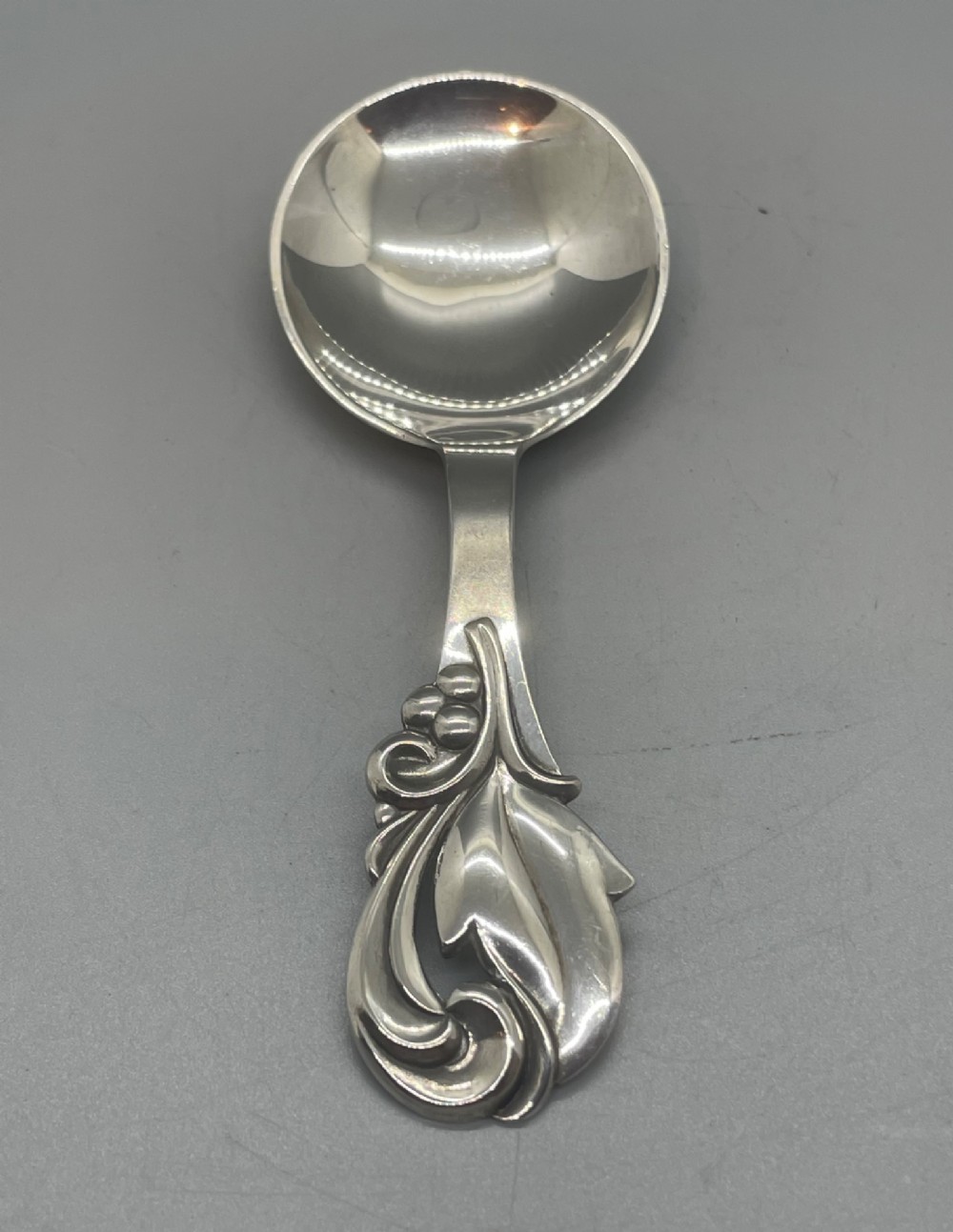 A vintage solid silver caddy spoon featuring a rounded bowl and an ornate leaf and scroll decorated handle. View III