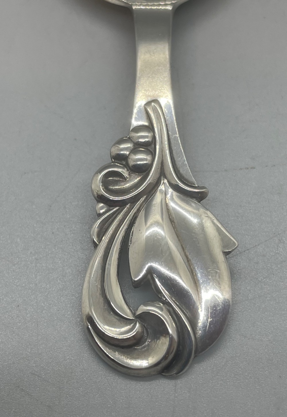 A vintage solid silver caddy spoon featuring a rounded bowl and an ornate leaf and scroll decorated handle. View IV