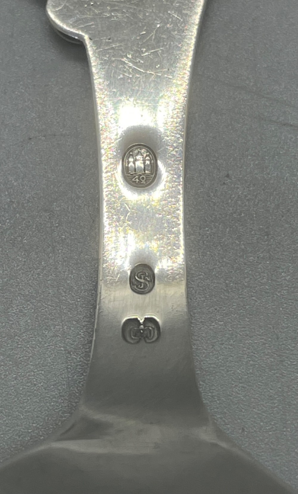 A vintage solid silver caddy spoon featuring a rounded bowl and an ornate leaf and scroll decorated handle. View V