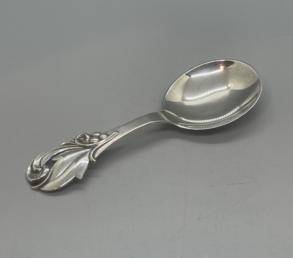 A vintage solid silver caddy spoon featuring a rounded bowl and an ornate leaf and scroll decorated handle. View VI