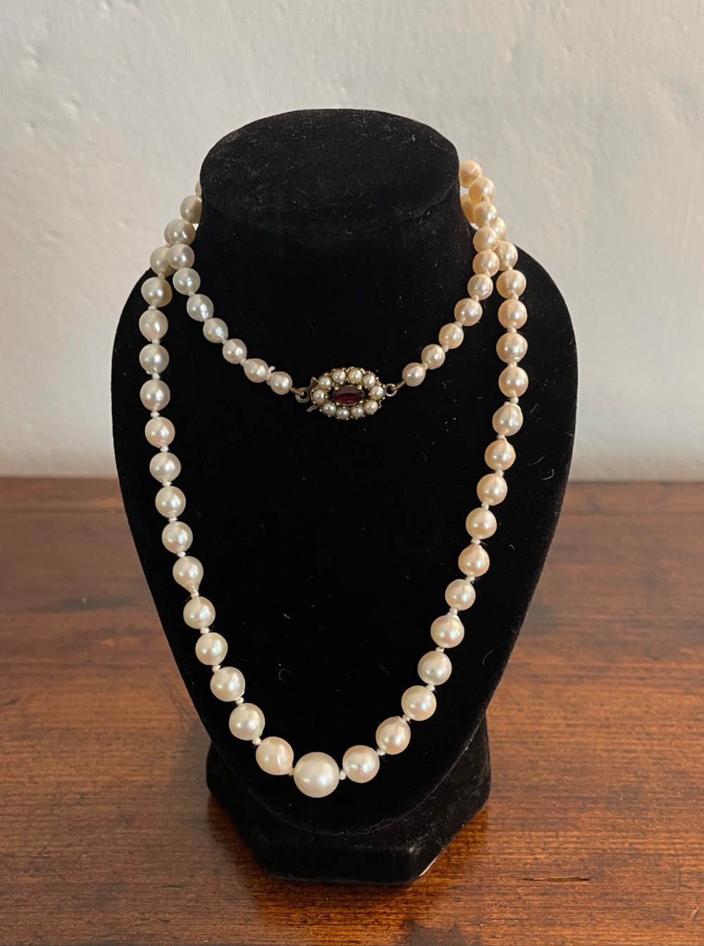 A strand of cream cultured pearls featuring a central oval red garnet clasp set in gold.