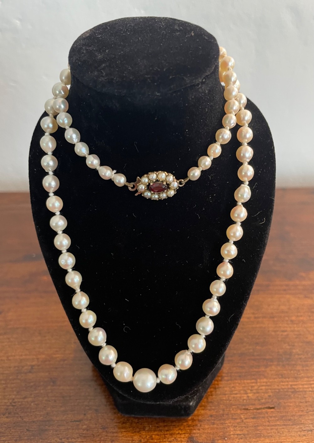 A strand of cream cultured pearls featuring a central oval red garnet clasp set in gold. View II