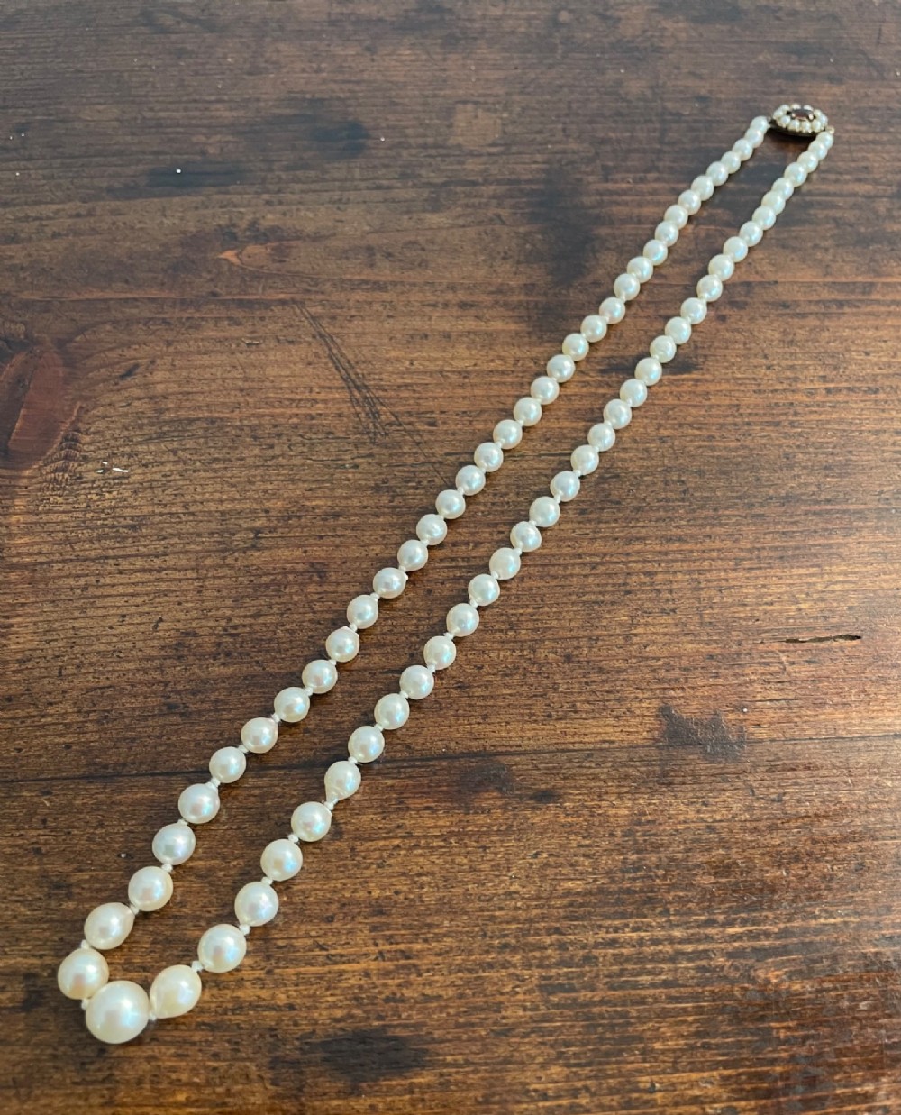 A strand of cream cultured pearls featuring a central oval red garnet clasp set in gold. View III