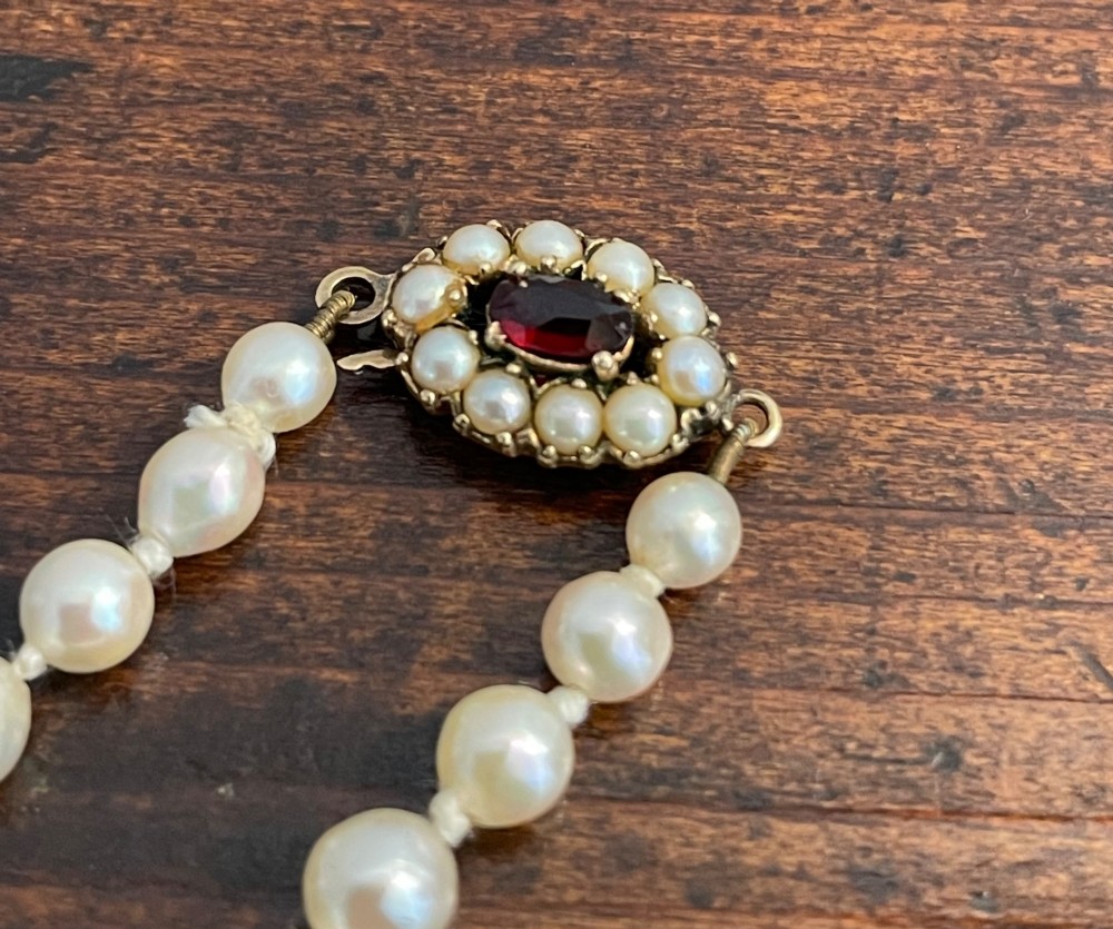 A strand of cream cultured pearls featuring a central oval red garnet clasp set in gold. View IV