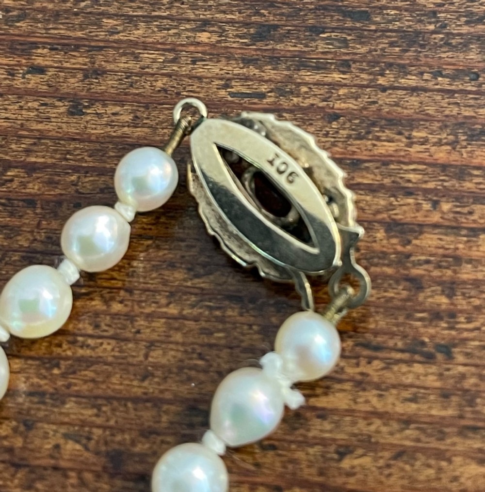 A strand of cream cultured pearls featuring a central oval red garnet clasp set in gold. View V