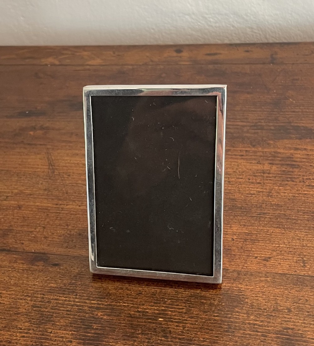 A small rectangular George V sterling silver photo frame with a plain polished border and dark fabric insertion. View II