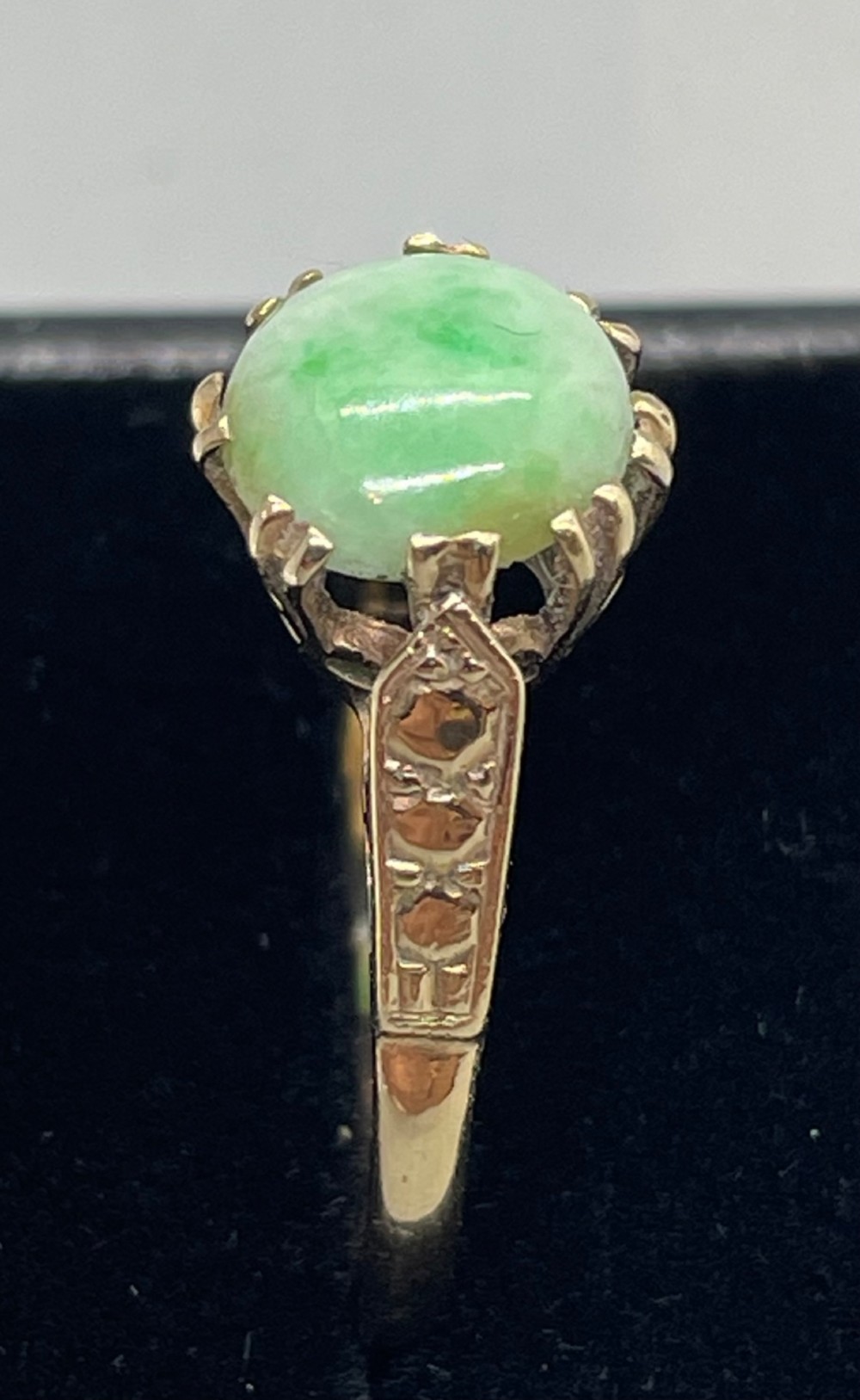 A vintage 9ct yellow gold ring featuring a polished round green jade cabochon in a multi-claw setting with geometric engraved shoulders. View II