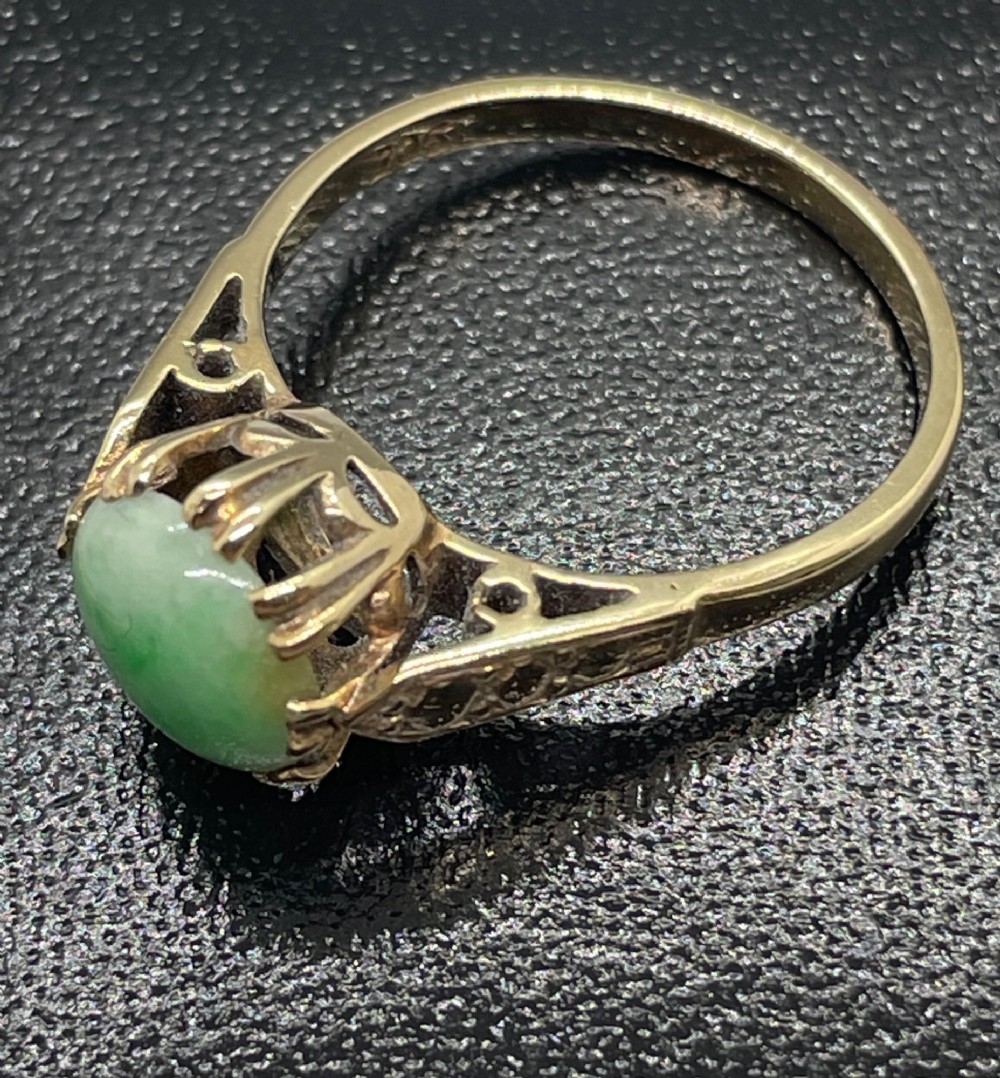 A vintage 9ct yellow gold ring featuring a polished round green jade cabochon in a multi-claw setting with geometric engraved shoulders. View V
