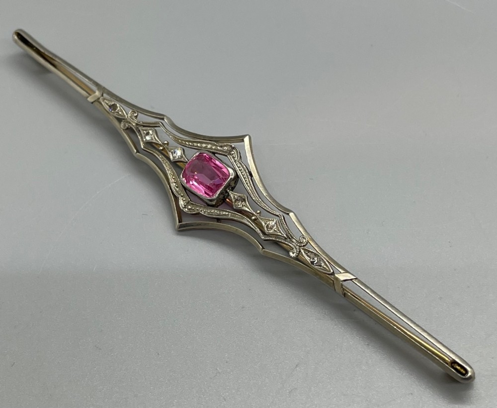 An Edwardian silver gilt bar brooch featuring geometric openwork filigree and a central cushion-cut pink paste stone. View II