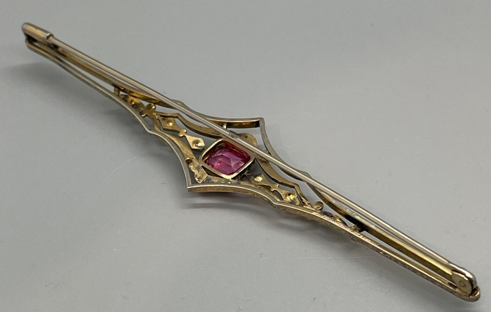 An Edwardian silver gilt bar brooch featuring geometric openwork filigree and a central cushion-cut pink paste stone. View III