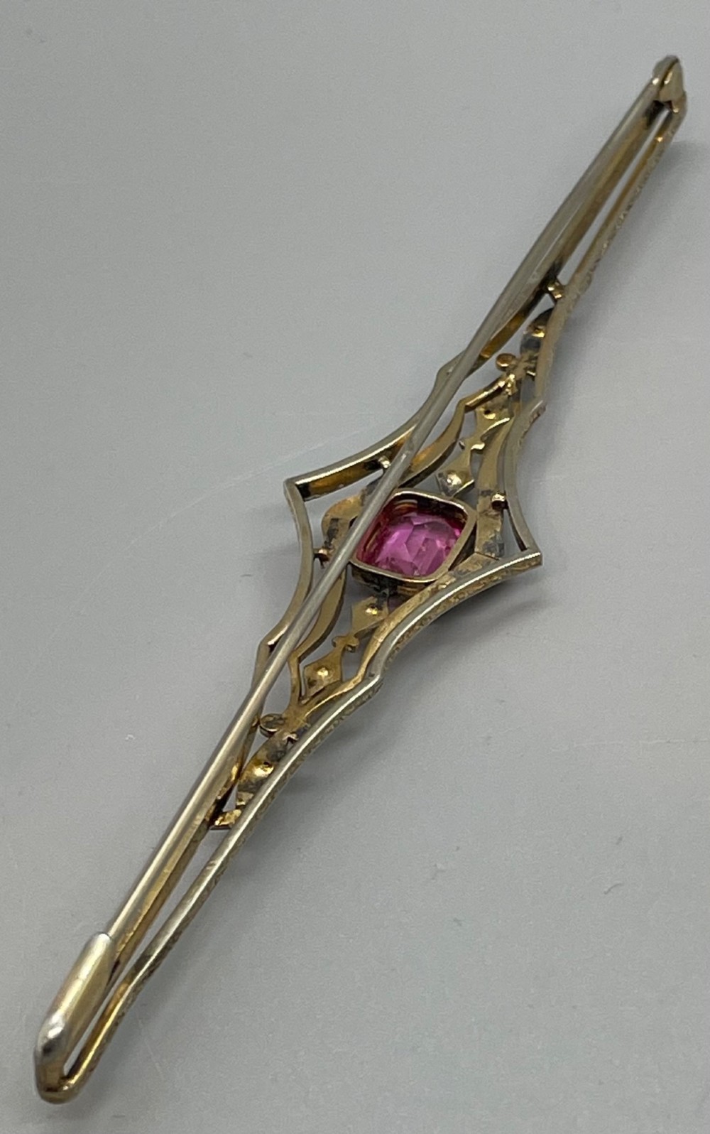 An Edwardian silver gilt bar brooch featuring geometric openwork filigree and a central cushion-cut pink paste stone. View IV