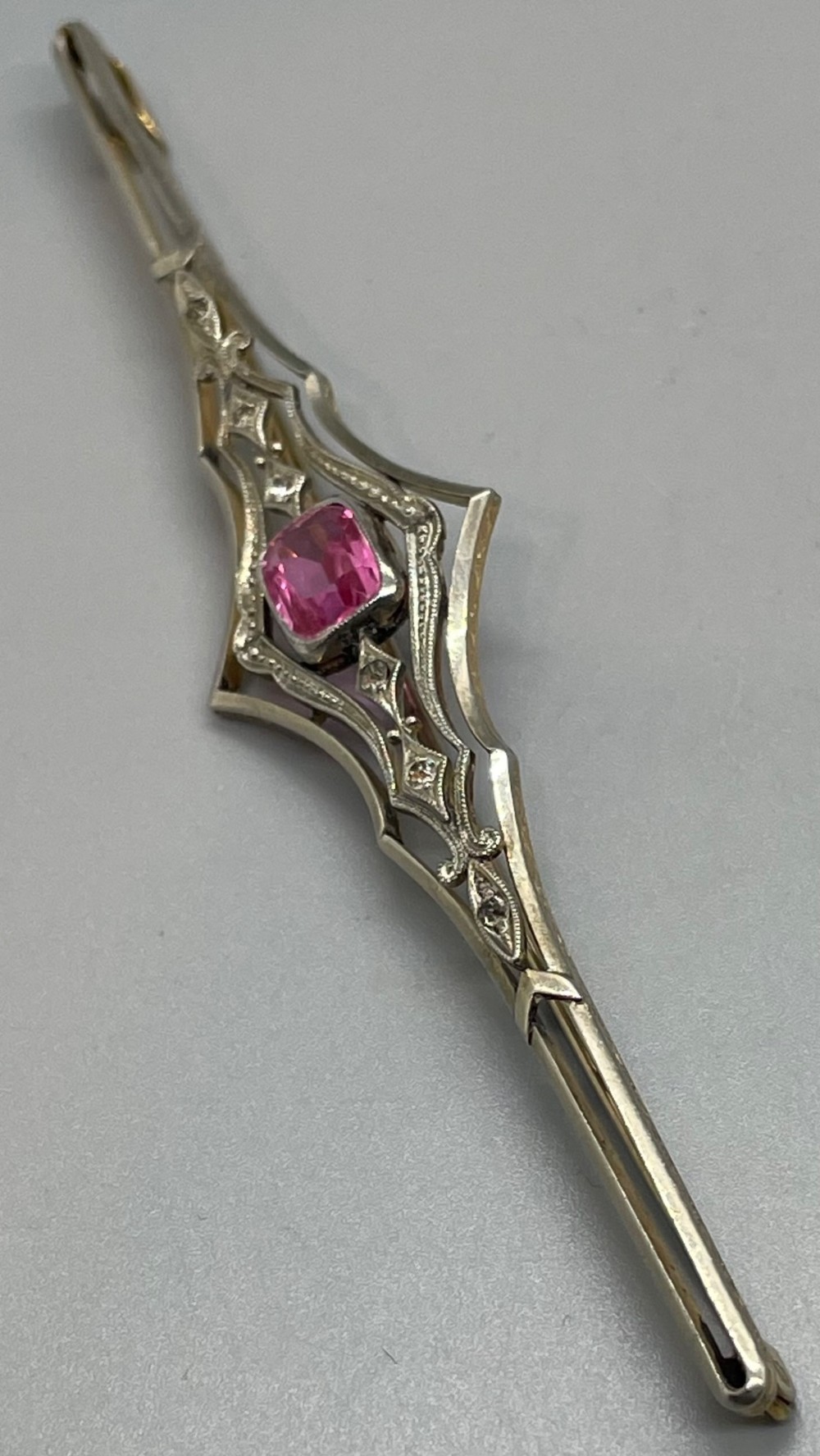 An Edwardian silver gilt bar brooch featuring geometric openwork filigree and a central cushion-cut pink paste stone. View V