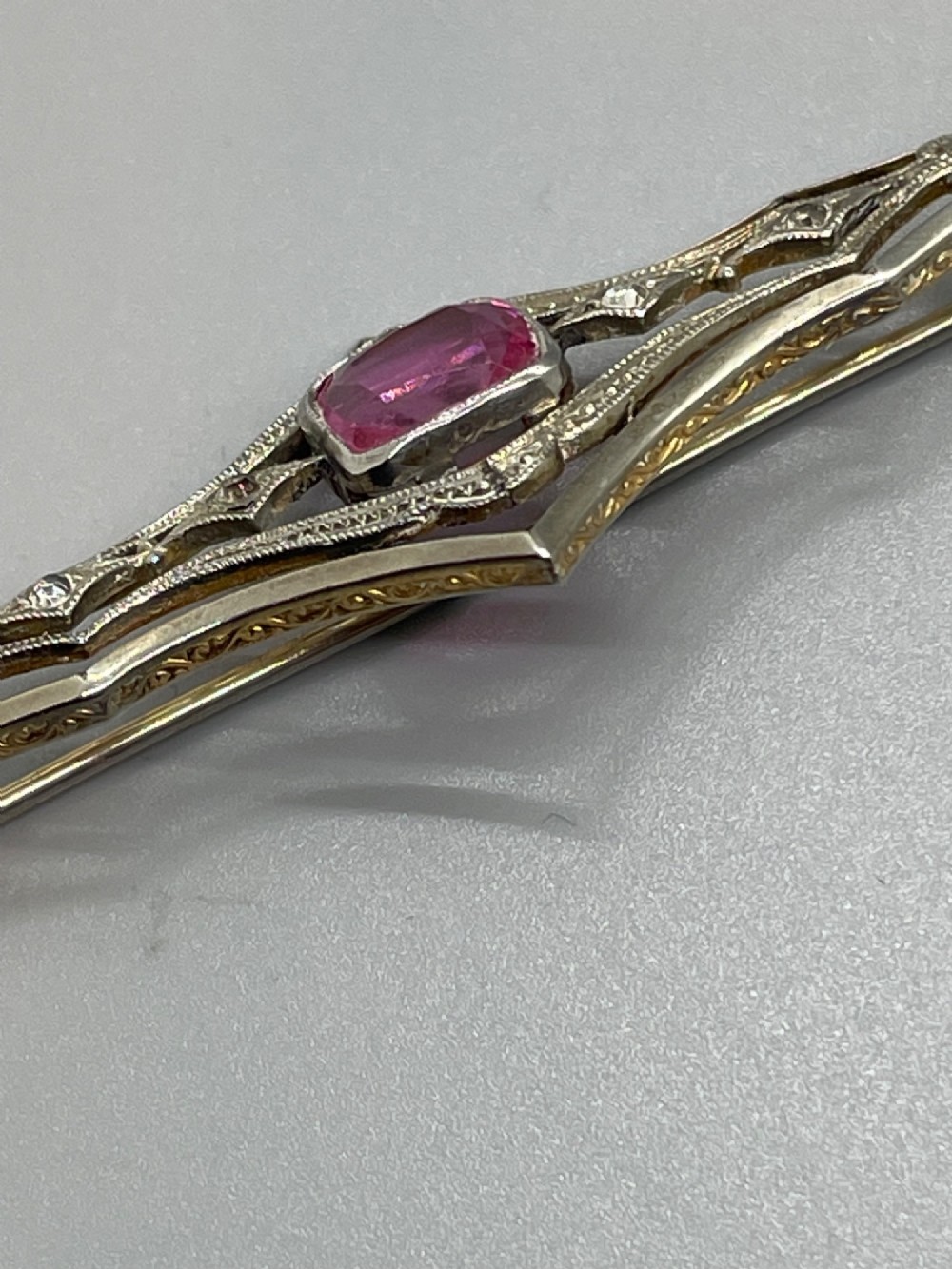 An Edwardian silver gilt bar brooch featuring geometric openwork filigree and a central cushion-cut pink paste stone. View VI