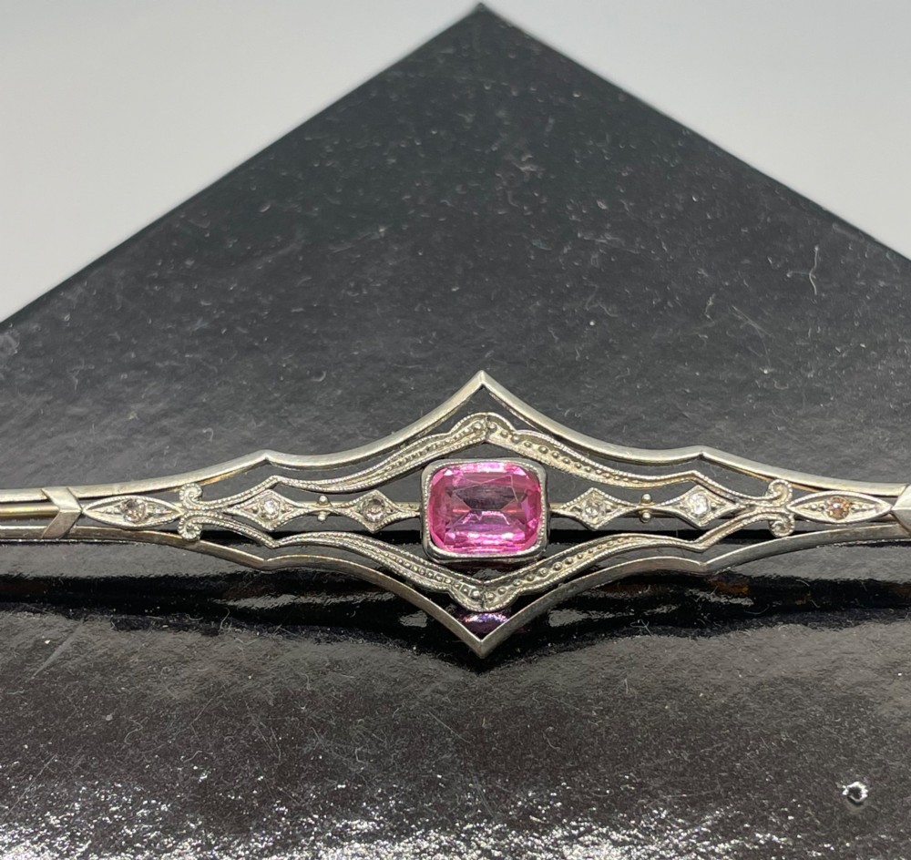An Edwardian silver gilt bar brooch featuring geometric openwork filigree and a central cushion-cut pink paste stone. View VII