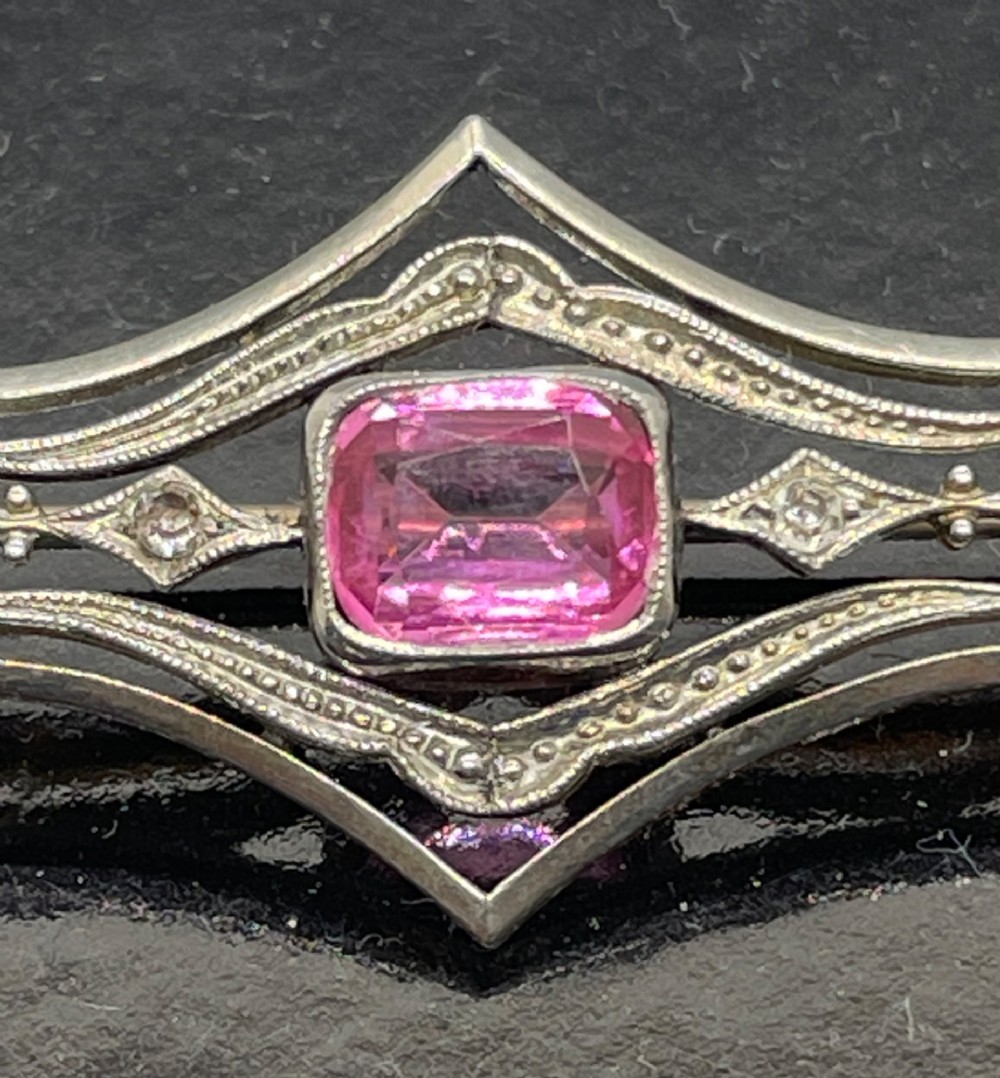 An Edwardian silver gilt bar brooch featuring geometric openwork filigree and a central cushion-cut pink paste stone. View VIII