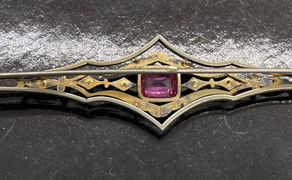 An Edwardian silver gilt bar brooch featuring geometric openwork filigree and a central cushion-cut pink paste stone. View IX