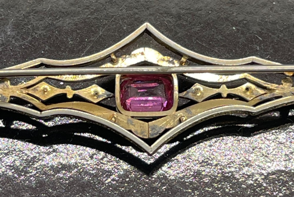 An Edwardian silver gilt bar brooch featuring geometric openwork filigree and a central cushion-cut pink paste stone. View X